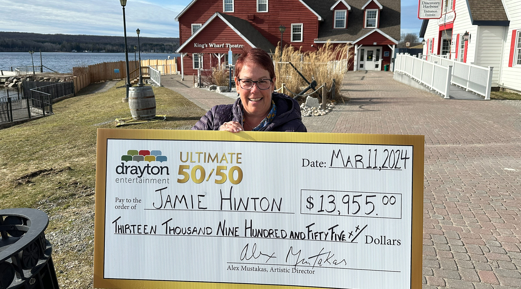 50/50 winner Jamie Hinton holding a big winner's cheque outside King's Wharf Theatre